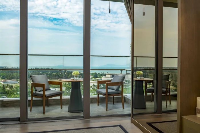 Ban công kính có bàn ghế thư giãn của căn hộ Hoiana Residences, phía xa là biển