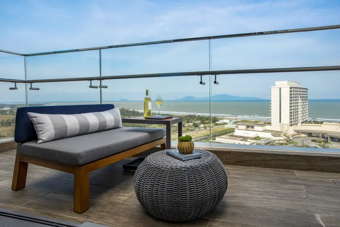 Ban công căn hộ Hoiana Residences với sofa ngoài trời, nhìn ra biển và khách sạn ven bờ